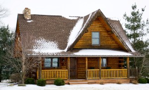 A log cabin with snow on the roof and porch rails.